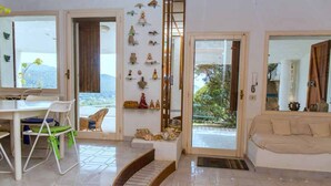 A bright living room with a white sofa, a dining area with a table and chairs, and a view of the outdoors through the glass door. - Luxury Beach Escape, Sea View Hottub,cinema Lounge (Maracalagonis)