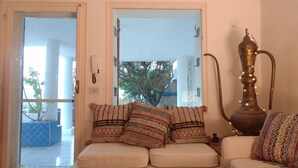A cozy living room with a sofa, patterned cushions, a decorative metal vase, and a view of the outdoors through a glass door. - Luxury Beach Escape, Sea View Hottub,cinema Lounge (Maracalagonis)