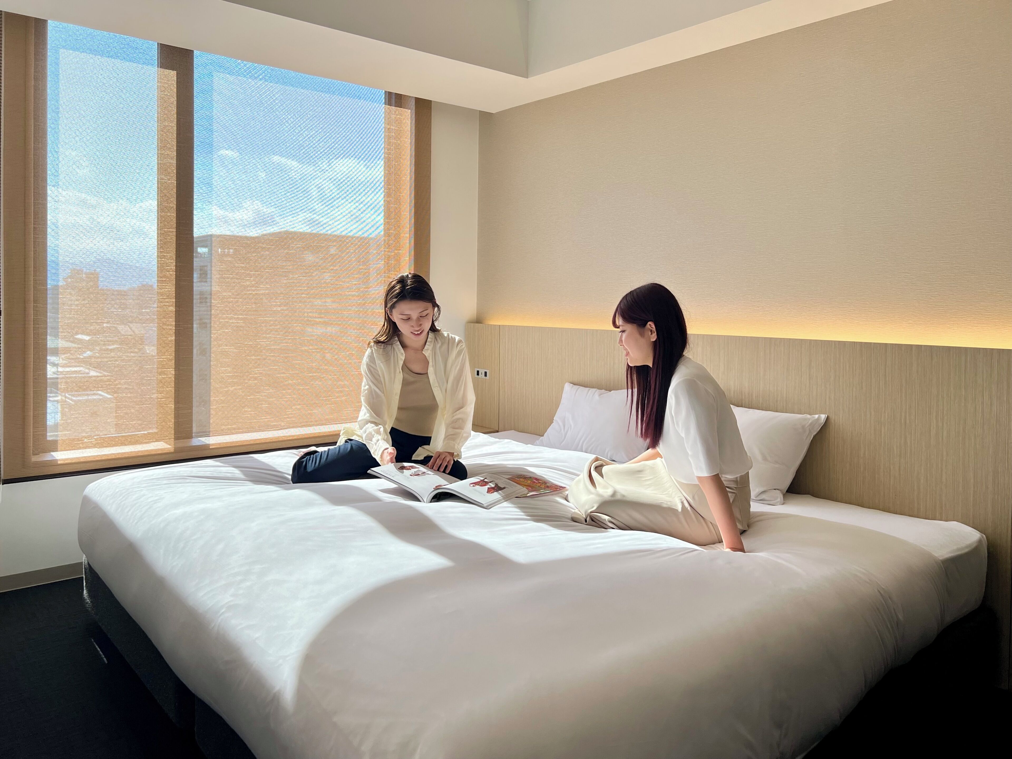 Habitación de hotel con una cama grande, ventana con persianas y vistas a edificios.