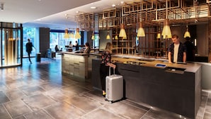 Un área de recepción moderna con un mostrador central, estanterías de madera en el techo e iluminación colgante.