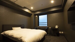 Een hotelkamer met een groot bed, een stoel, een klein tafeltje en een raam met uitzicht.