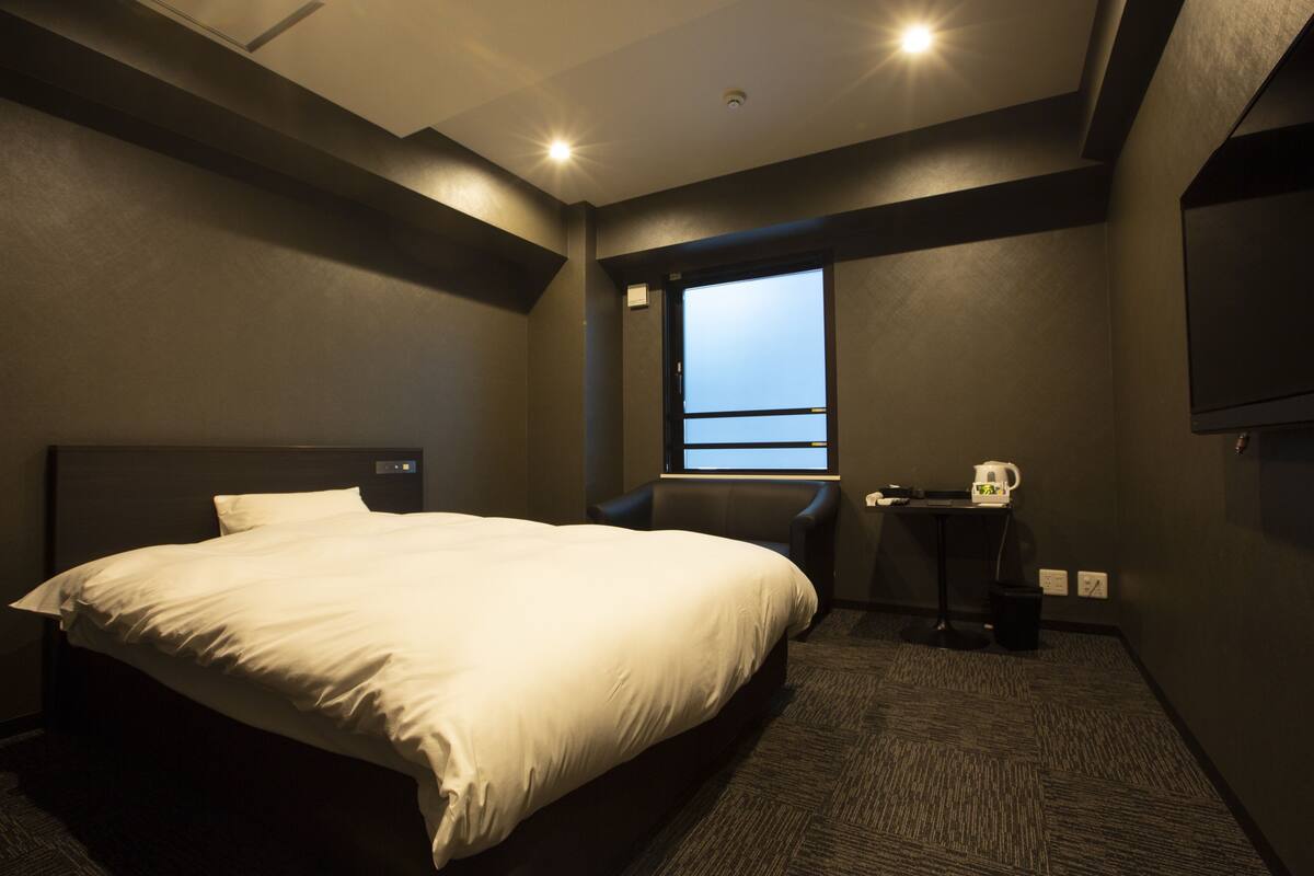 A hotel room with a large bed, a chair, a small table, and a window with a view.