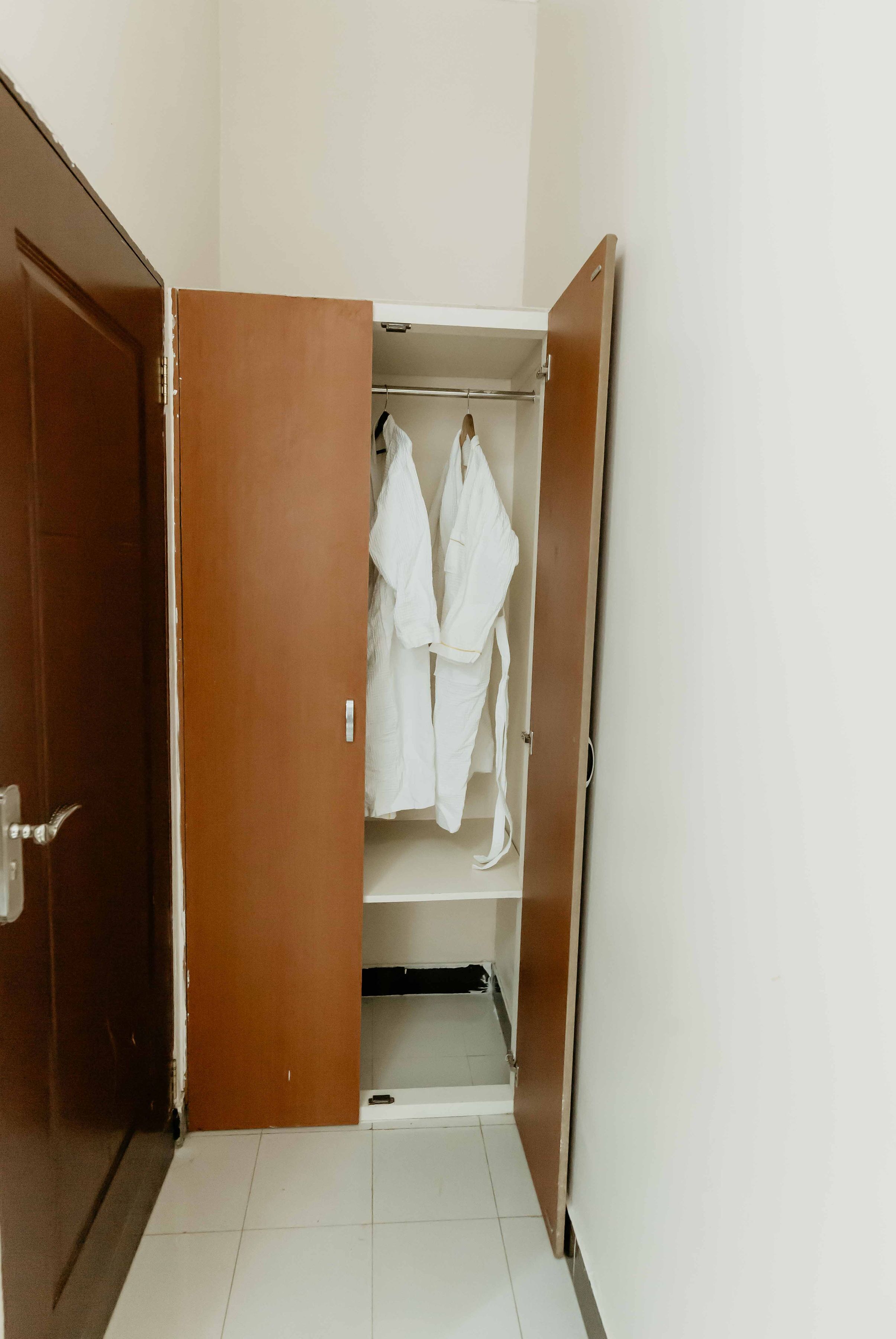 Ein Hotelzimmer mit einem Holzschrank, einem weißen Bademantel darin und einem gefliesten Boden.