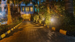 A pathway leading to a building with a balcony, surrounded by greenery and a paved walkway. - Panama Garden Resort (Moshi)