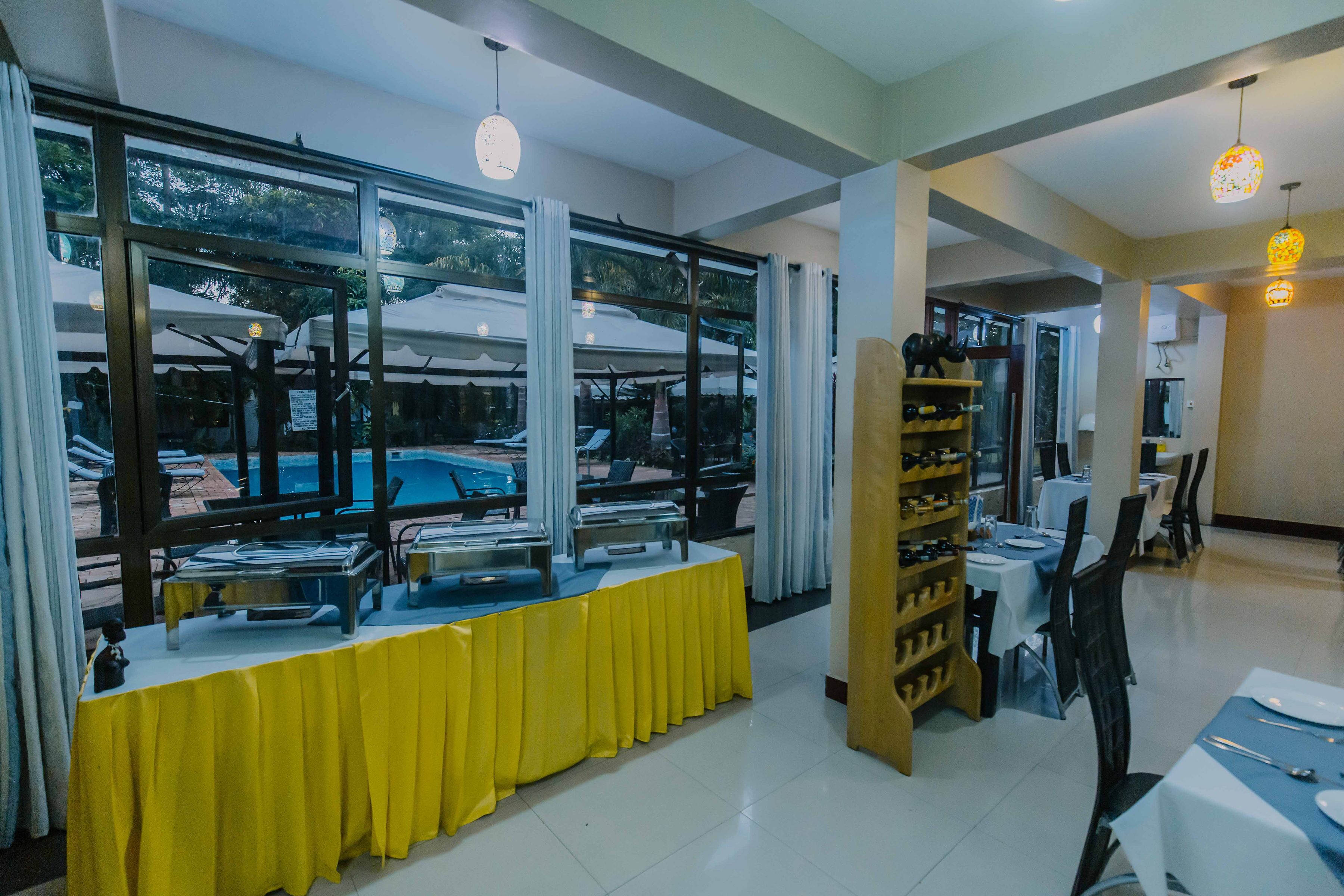 A dining area with a buffet table covered in yellow, large windows, and a wine rack.