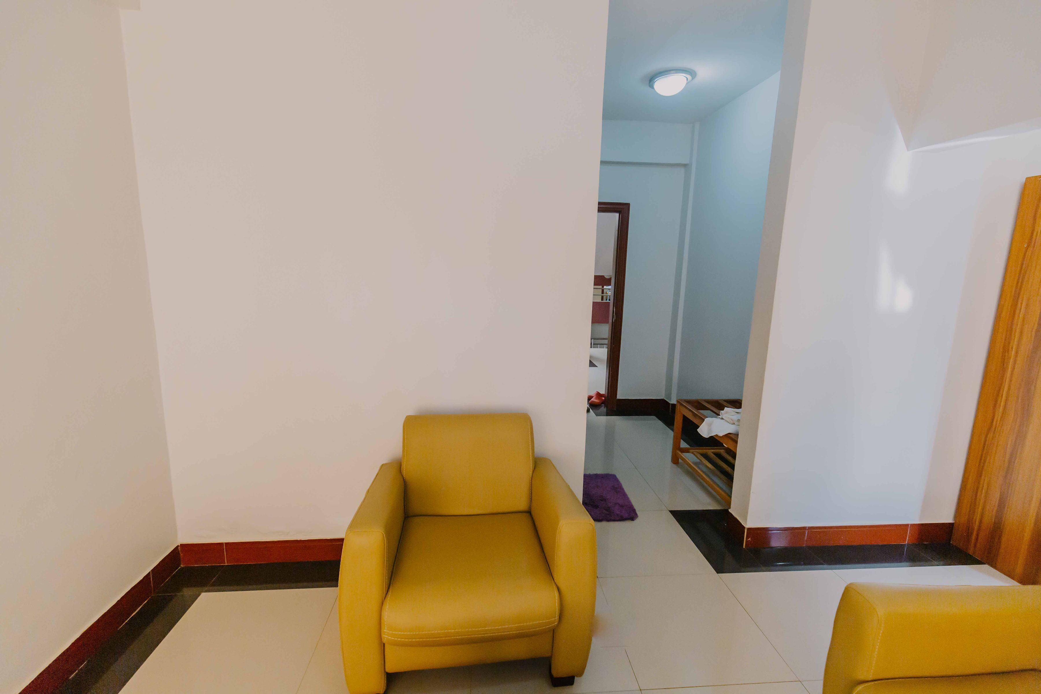A room with a yellow armchair, a wooden door, and a tiled floor.