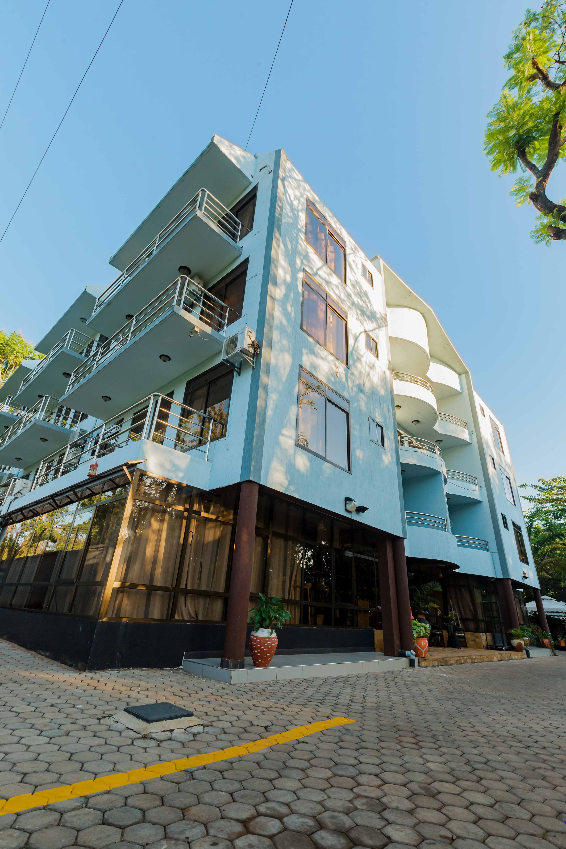 A multi-story building with balconies, large windows, and a paved entrance area with potted plants.