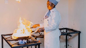 A chef in a white uniform with a blue hat cooking on a gas stove. - Panama Garden Resort (Moshi)