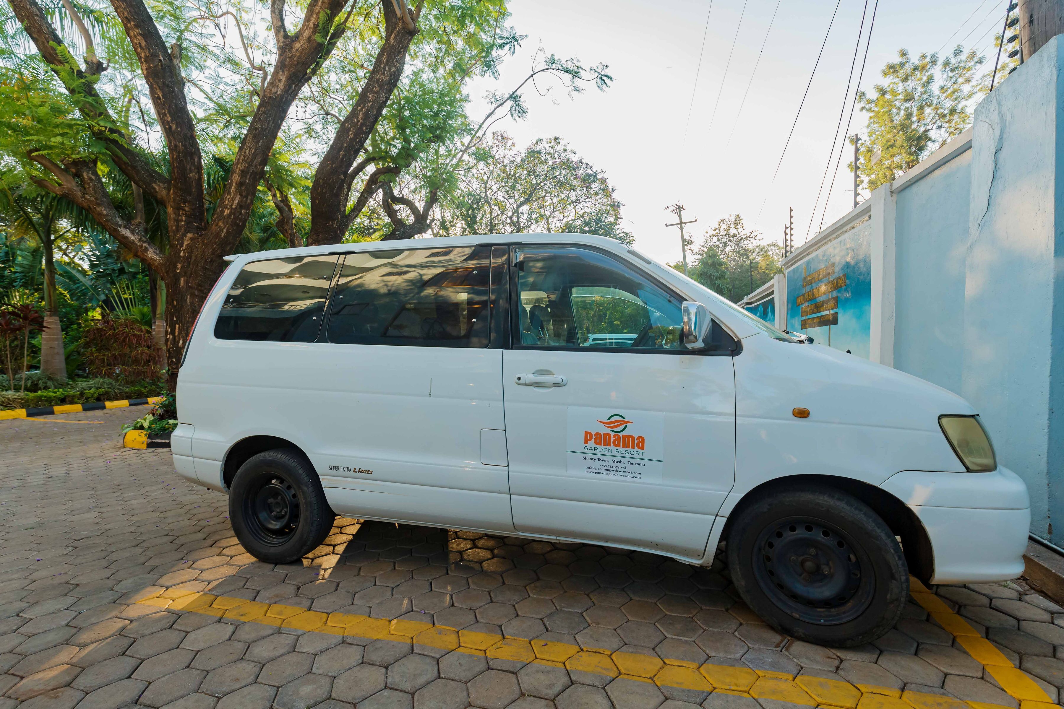 A white van parked on a paved area with yellow lines, near a blue wall with a sign that reads "Panama Garden Resort."