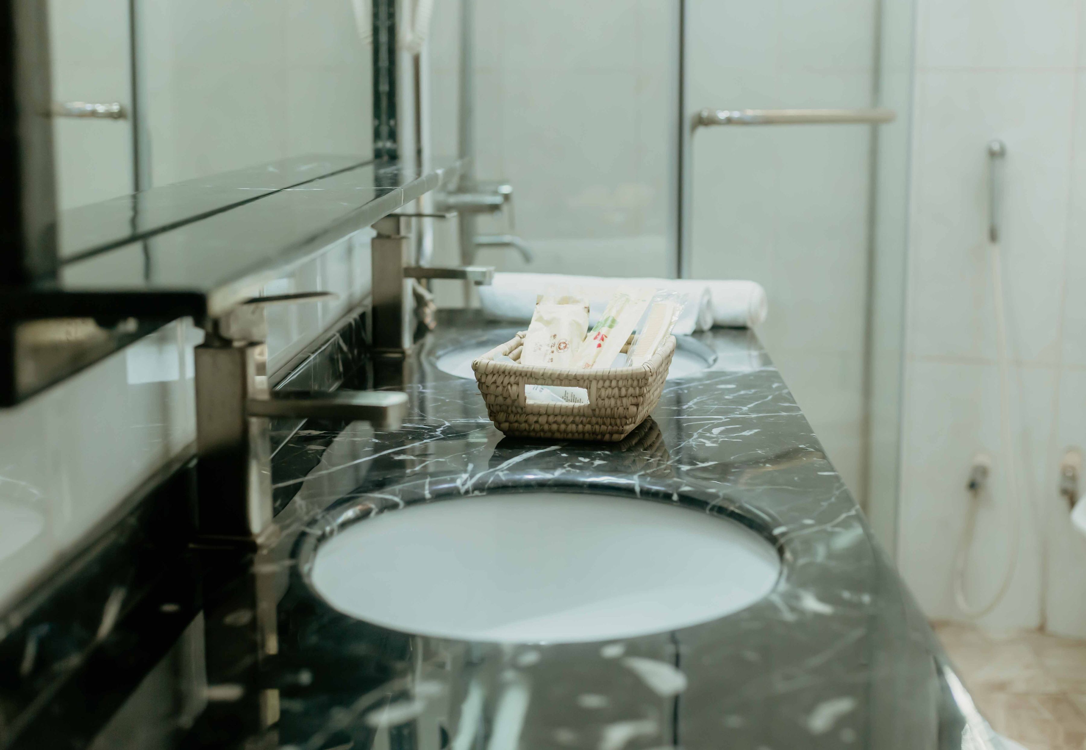 A bathroom with a black marble sink, a wicker basket with toiletries, and a towel dispenser.