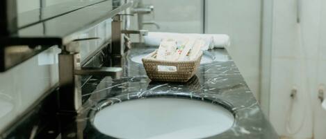 A bathroom with a black marble sink, a wicker basket with toiletries, and a towel dispenser.