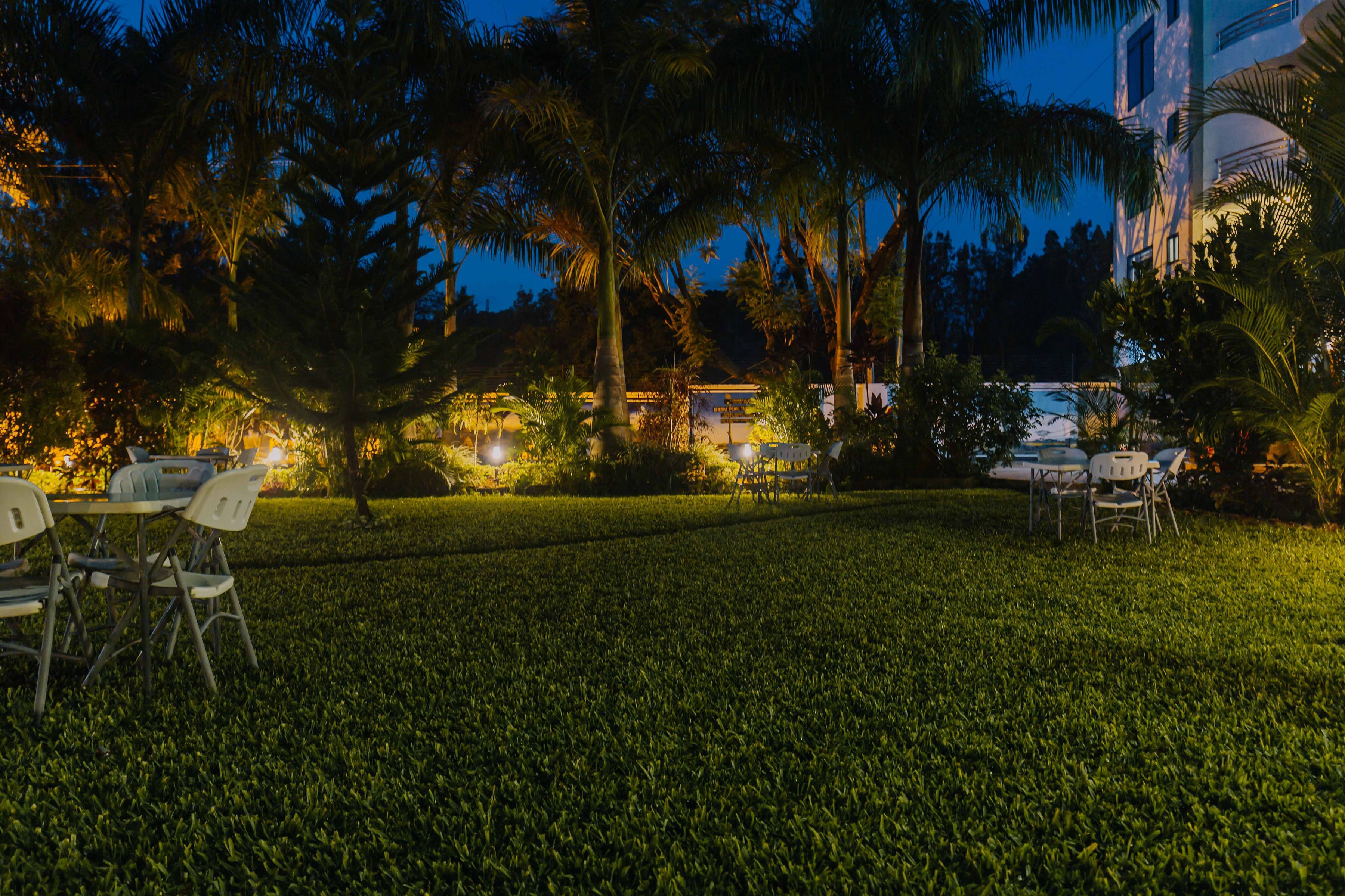 A well-lit outdoor seating area with tables and chairs, surrounded by lush greenery and palm trees.