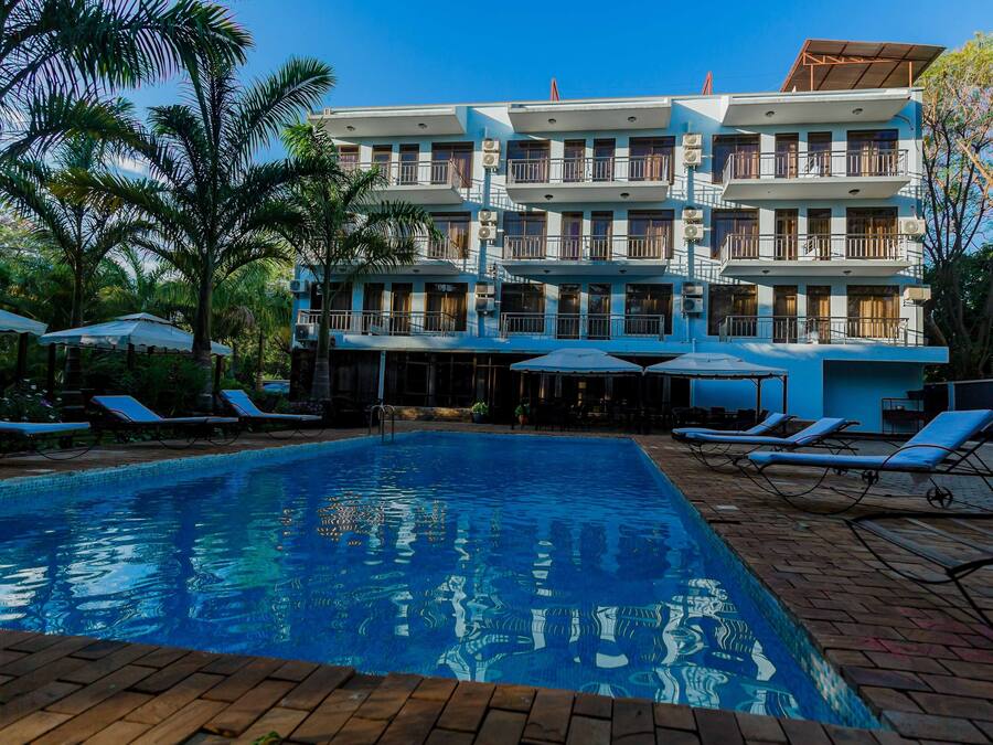A hotel with a swimming pool, sun loungers, and a multi-story building with balconies.