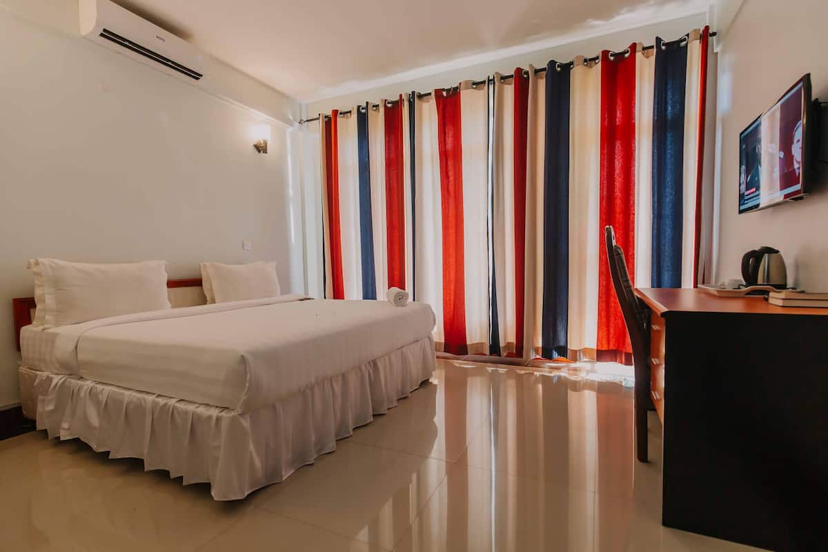 Une chambre d’hôtel équipée d’un lit, d’un bureau, d’une chaise, d’une télévision et d’un rideau à motifs rayés.