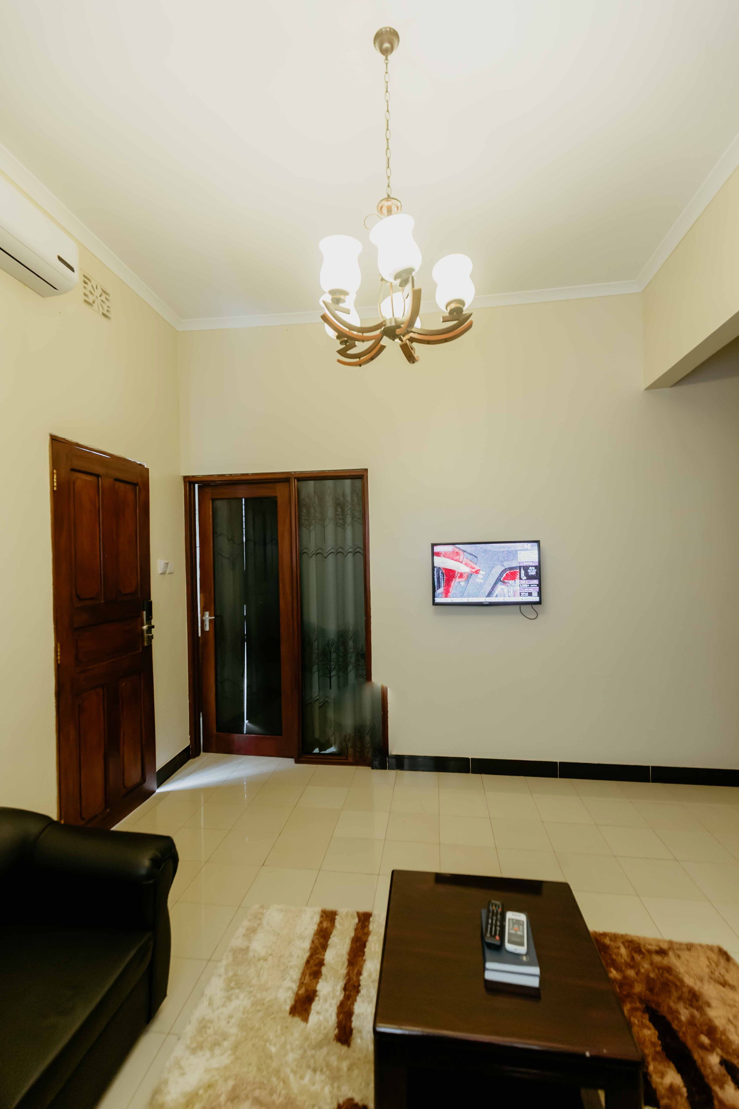 A living room with a chandelier, a television mounted on the wall, a sofa, and a coffee table.