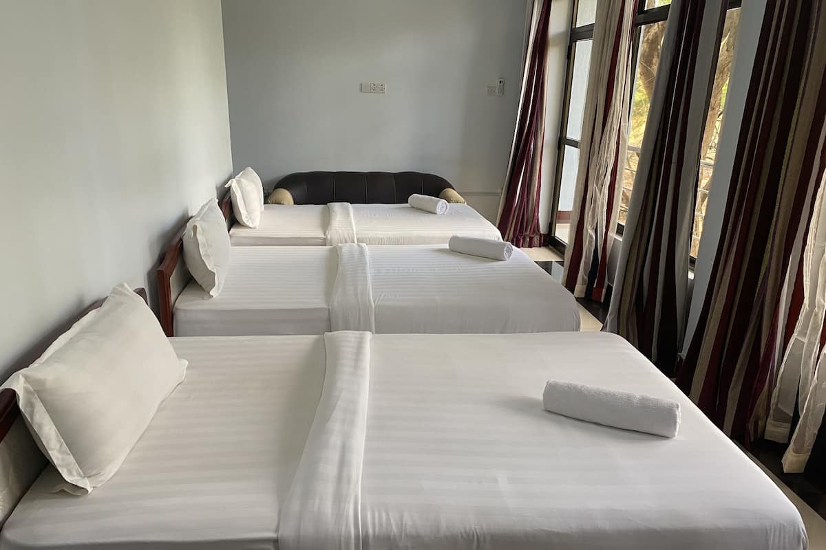 Une chambre d’hôtel avec trois lits, chacun doté de draps et d’oreillers blancs, et une fenêtre avec des rideaux à rayures.