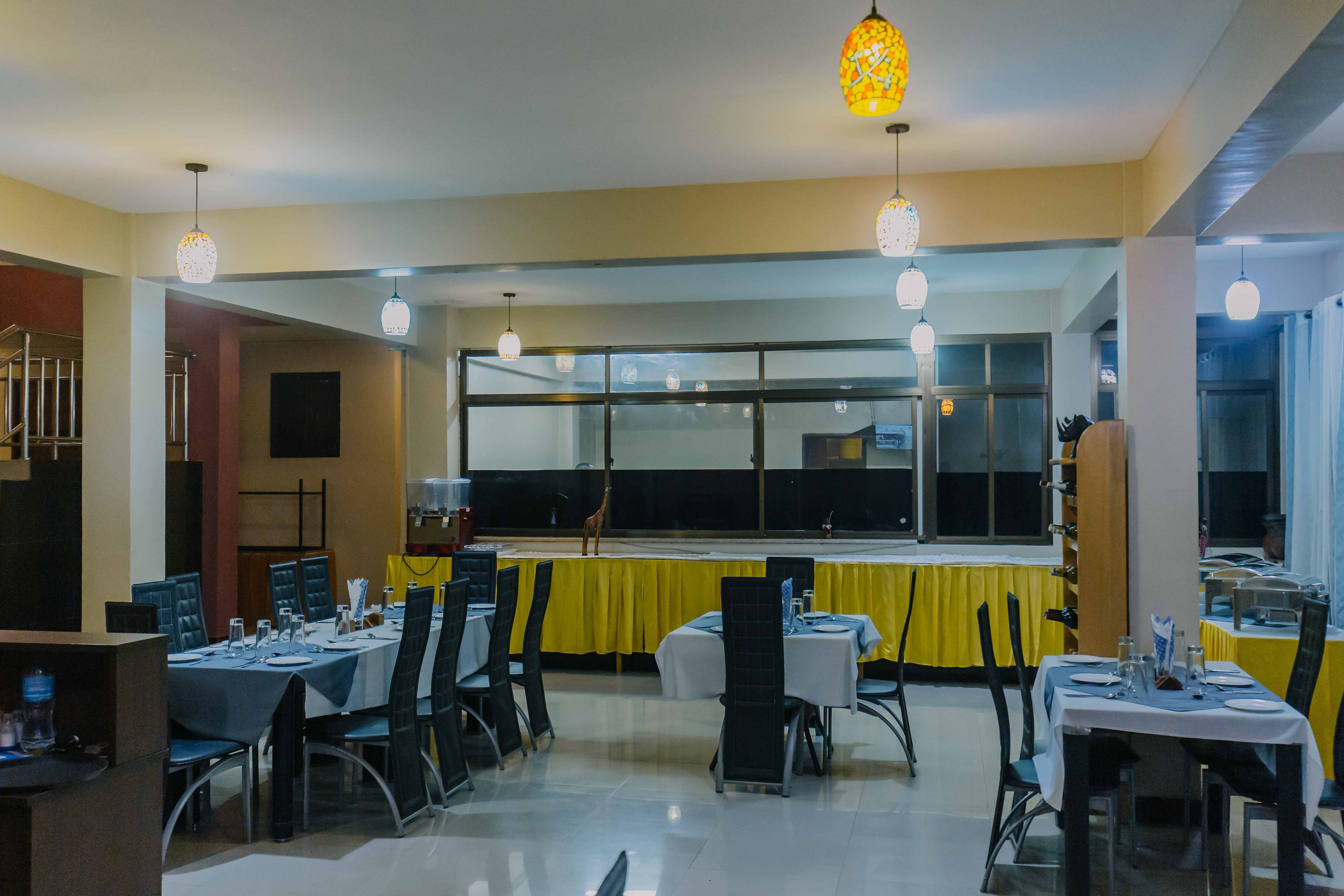 A dining area with tables set for meals, chairs, and hanging pendant lights.