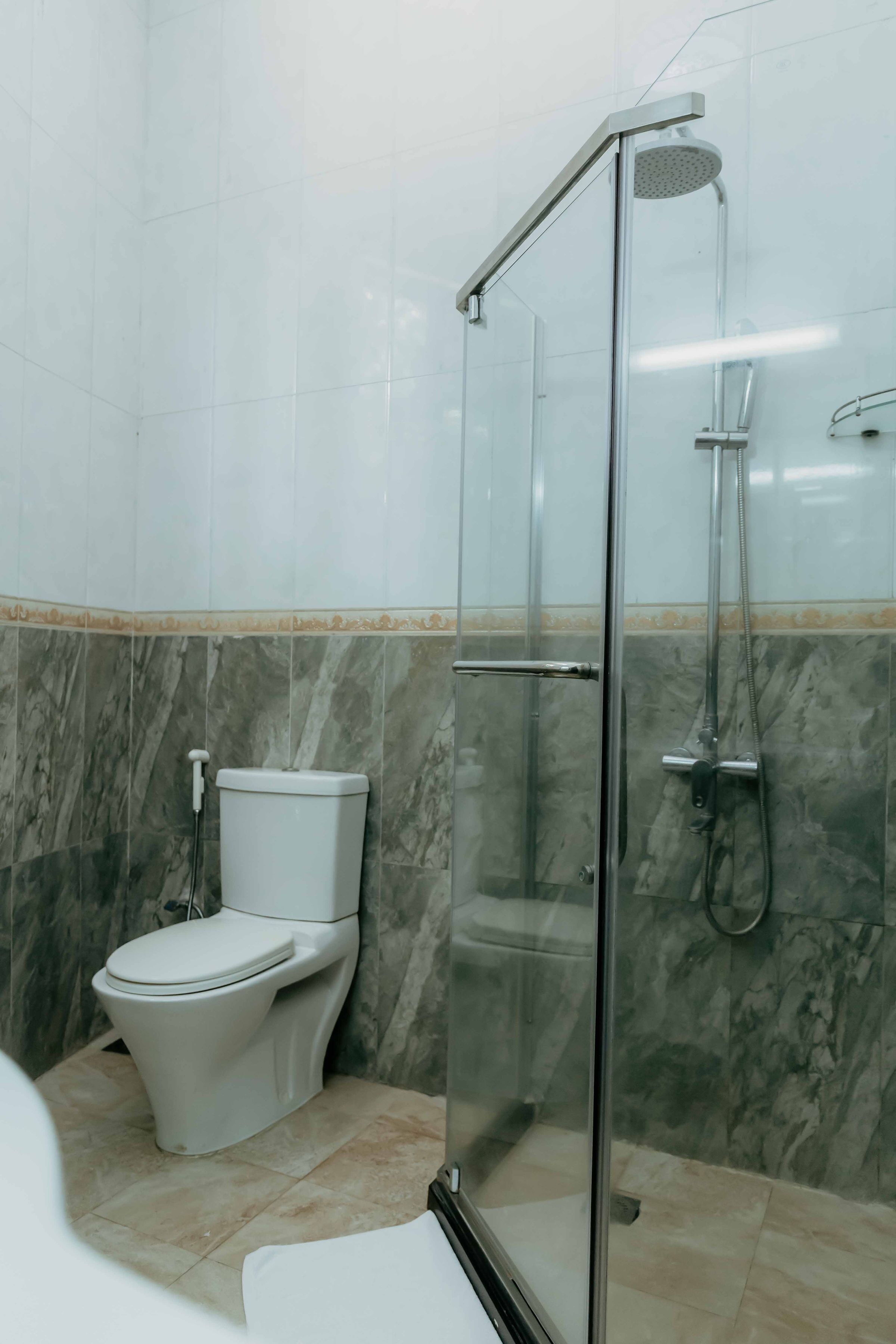 A bathroom with a glass-enclosed shower, a toilet, and marble tiles.