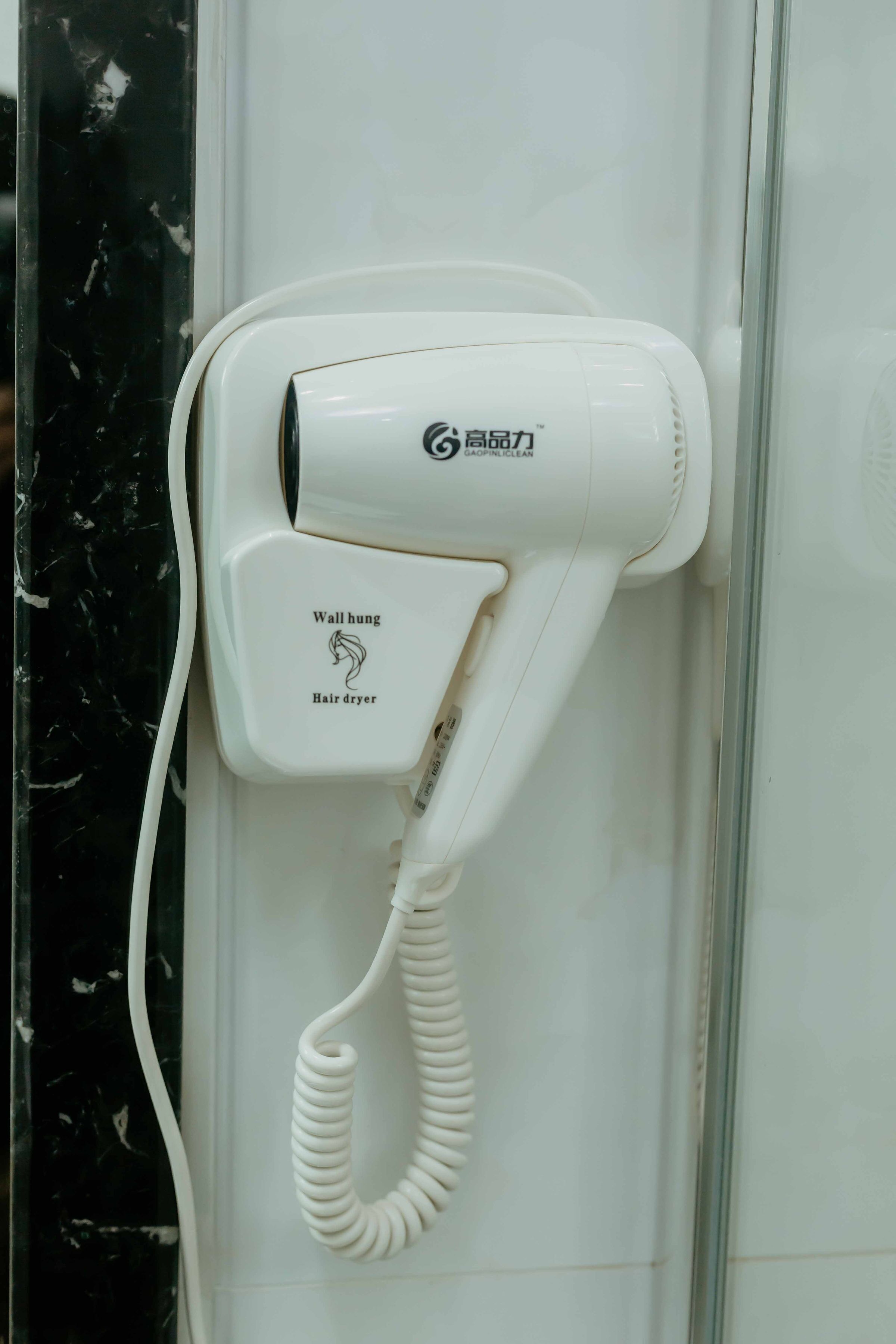 A wall-mounted hair dryer with a cord, labeled "Wall hung Hair dryer," attached to a bathroom wall.