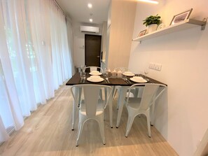 Uma sala de jantar com mesa posta para quatro, cadeiras brancas e uma estante com planta e quadro.