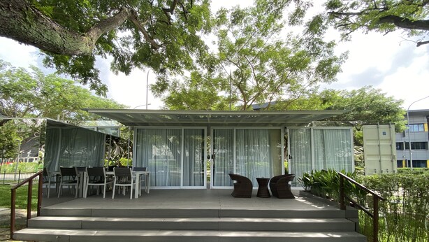 A covered outdoor seating area with steps leading up to it, surrounded by greenery and trees. - Shipping Container Hotel @ One-North (Singapore)