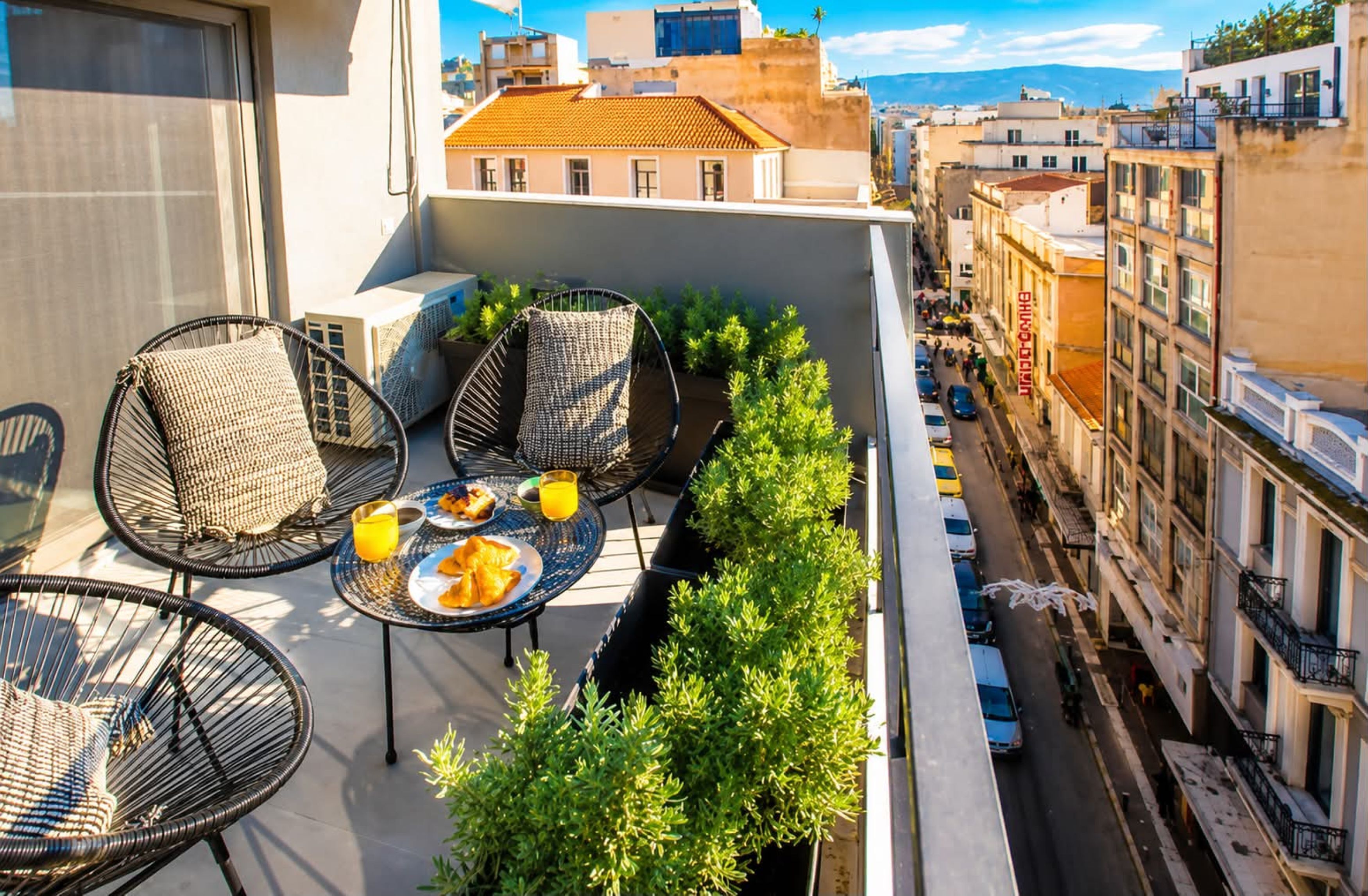Une terrasse sur le toit, avec des fauteuils en osier, une table garnie de nourriture et de boissons, et une vue sur le paysage urbain.