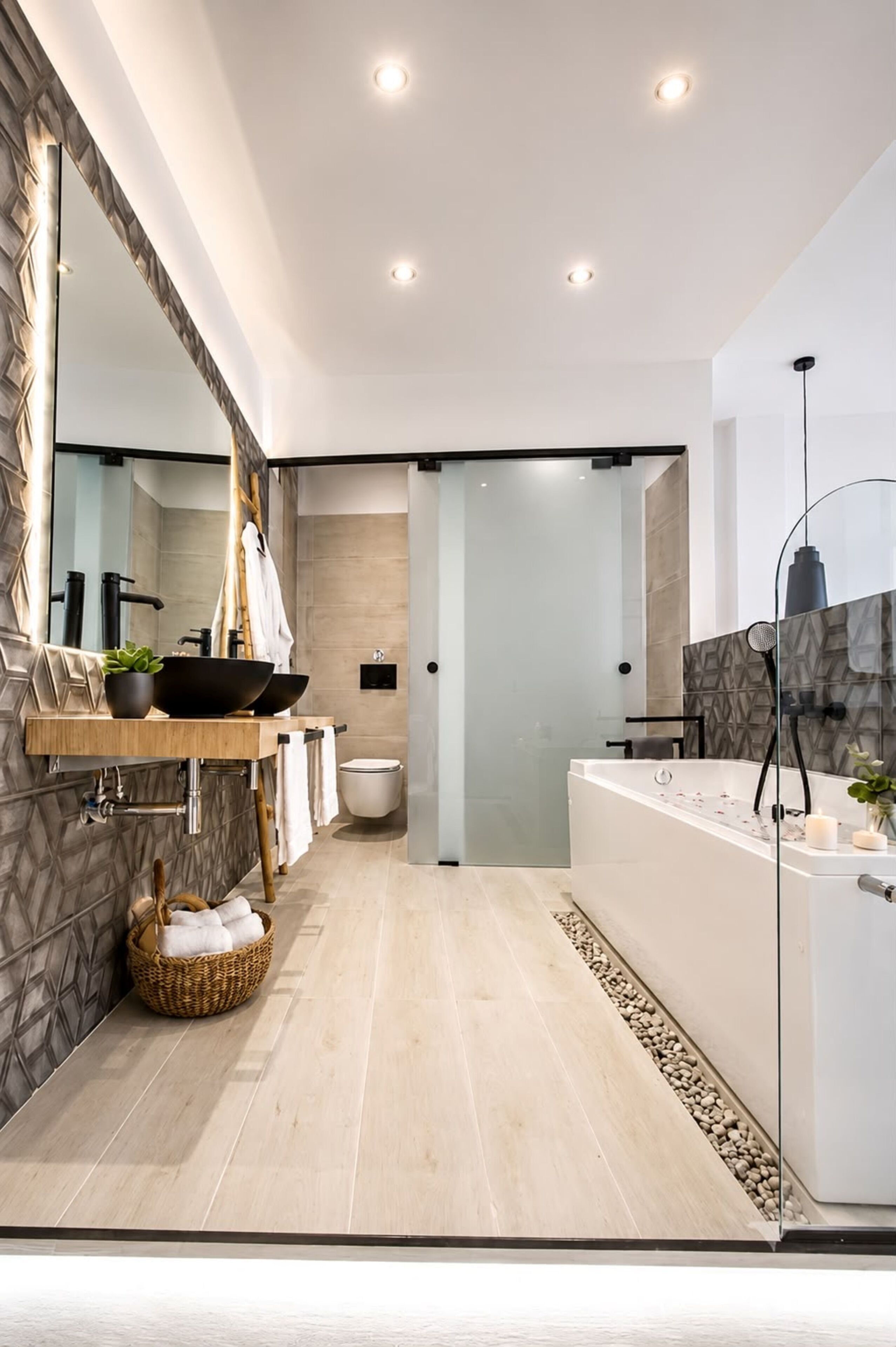 Un baño moderno con un espejo grande, un lavamanos con un lavabo negro, un inodoro blanco y una bañera con cerramiento de vidrio.