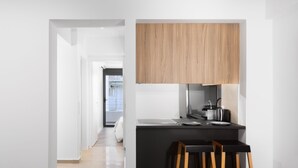 A modern kitchen with a black countertop, wooden cabinets, and a view into a bedroom. - Elysium Boutique Apartments (Zografos)