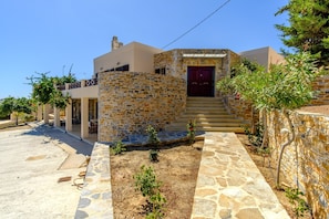 A stone-walled house with a red door, a small garden, and a paved driveway.