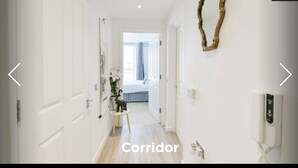 Un couloir aux murs blancs, avec un plancher en bois, et un lit visible au loin.