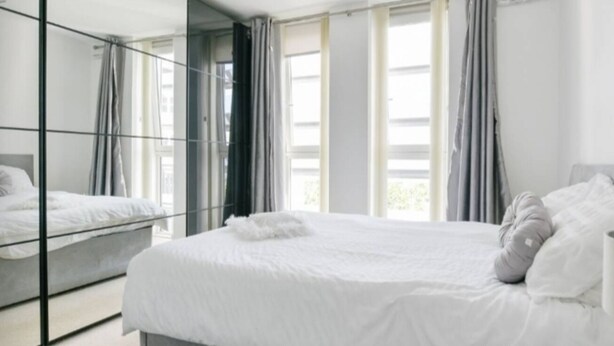 Une chambre moderne avec un grand lit, une armoire à miroir et de grandes fenêtres avec des rideaux.