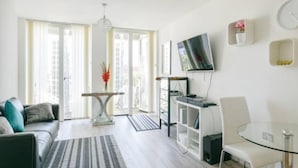 Un salon moderne avec un canapé, une table en verre, un téléviseur fixé au mur et un balcon offrant une vue dégagée.