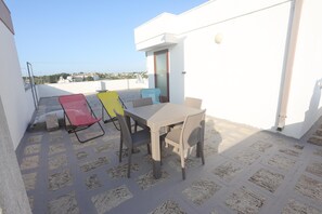 Eine Dachterrasse mit Tisch und Stühlen, einer Satellitenschüssel und einem weißen Gebäude im Hintergrund.
