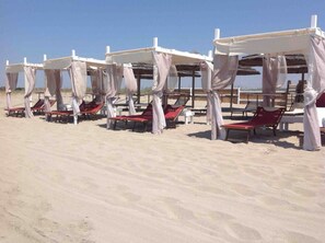 Une plage bordée de rangées de transats sous des parasols blancs.