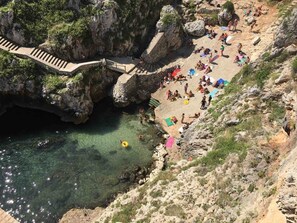 Ein felsiger Strand mit einer Stegbrücke zu einem Gebiet mit klarem Wasser.