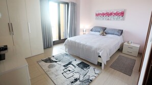 Quarto com cama, mesas de cabeceira, guarda-roupa e uma janela grande com cortinas.
