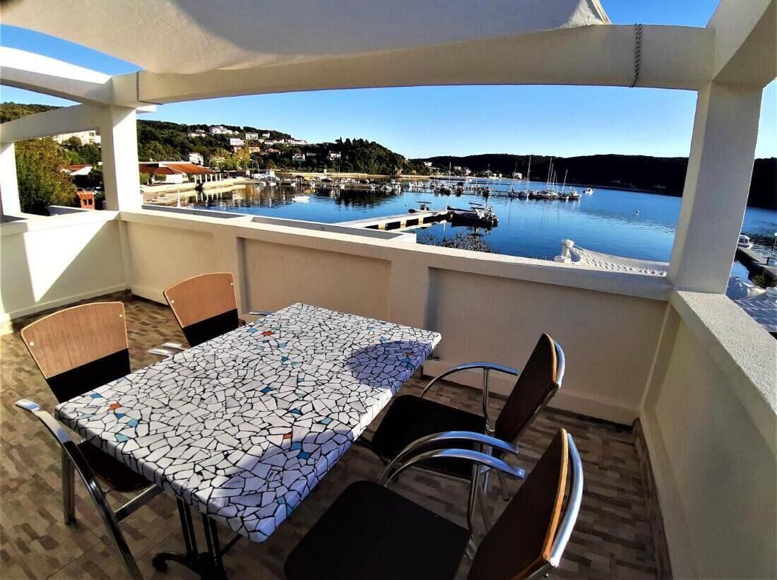 A terrace with a table and chairs, overlooking a marina with boats and houses in the background.