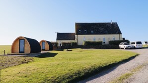A building with two small, round, wooden cabins and a larger building with a sloped roof. - Kirkapol Beach Sleeps 4 With Dog Access (Tiree Island)