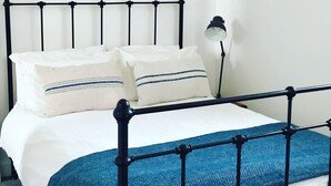 A bed with a metal frame, white bedding, and two pillows with blue stripes. - Kirkapol Beach Sleeps 4 With Dog Access (Tiree Island)