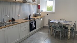 A kitchen with a built-in stove, a microwave, and a sink. There is a window with a view of greenery outside. - Kirkapol Beach Sleeps 4 With Dog Access (Tiree Island)
