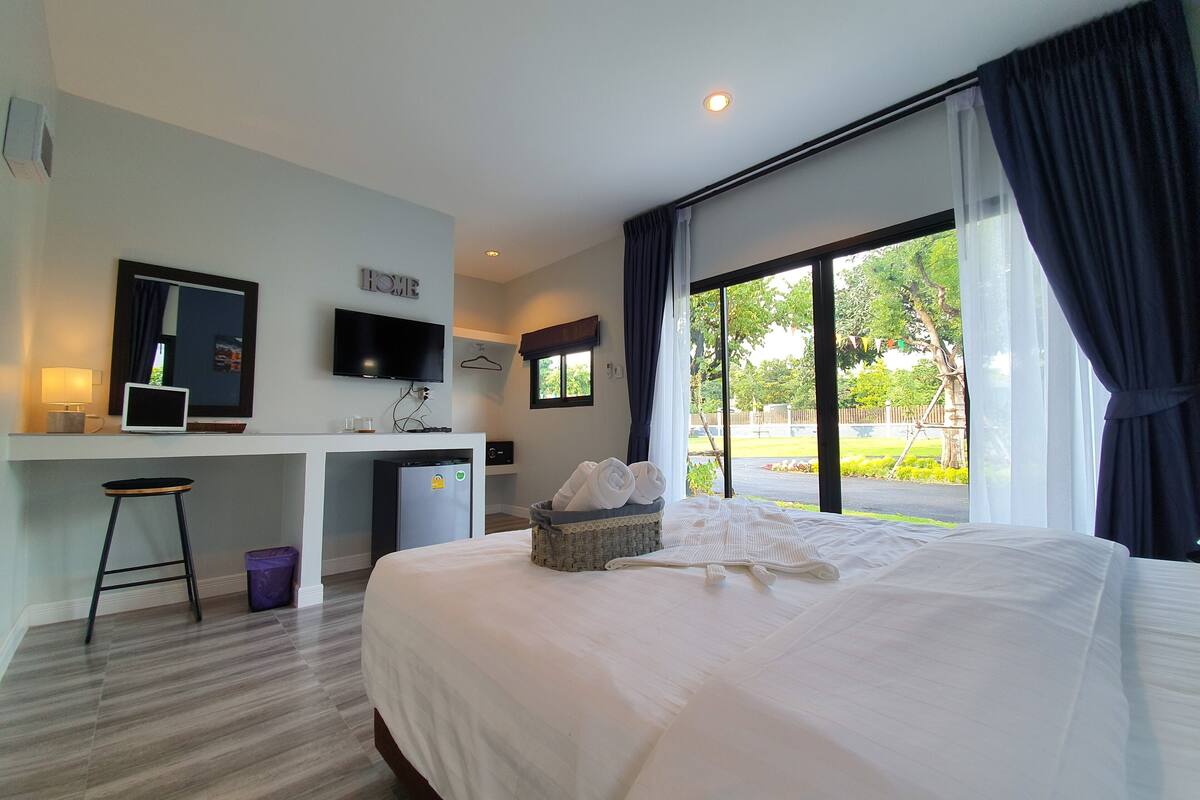 Quarto de hotel com cama, escrivaninha com computador, televisão e janela com cortinas.