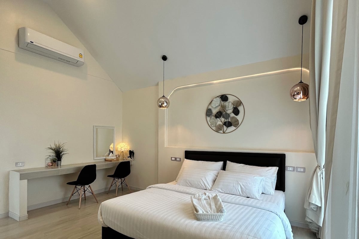 Quarto moderno com uma cama grande, uma escrivaninha, duas cadeiras, ar-condicionado fixado na parede e luminárias pendentes.