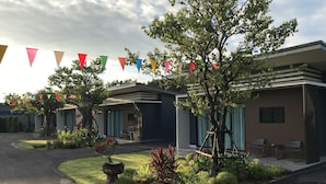 A modern hotel with a covered outdoor seating area, a landscaped garden, and colorful triangular flags. - Bannjamjuree Resort Sattahip (Sattahip)