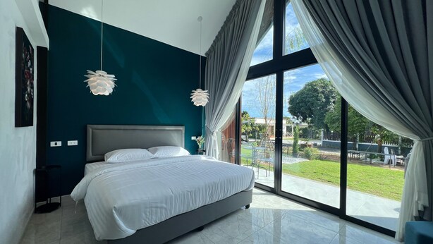 A modern bedroom with a large bed, a view of the outdoors, and a teal accent wall. - Bannjamjuree Resort Sattahip (Sattahip)