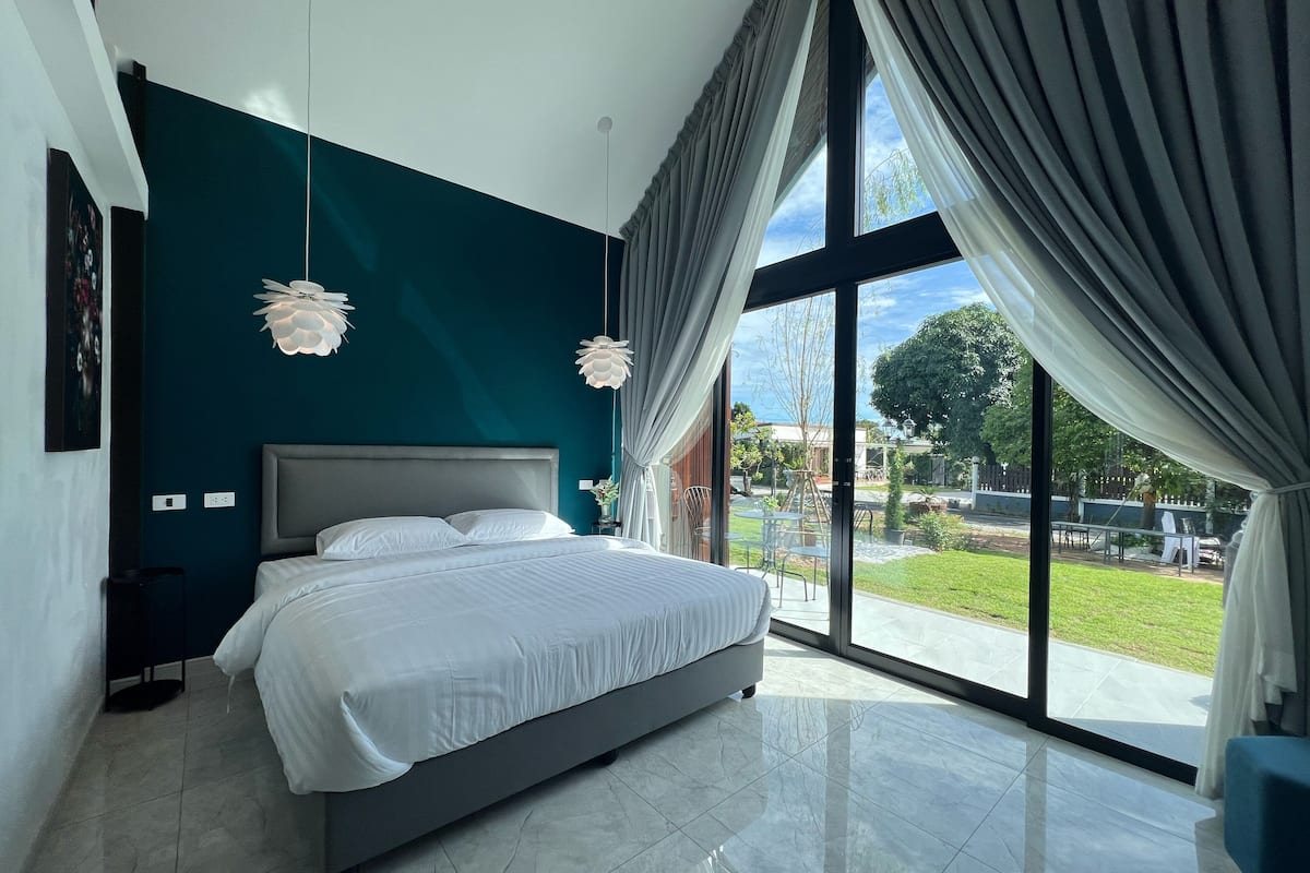 Quarto moderno com cama grande, vista para o exterior e parede de destaque em tom de verde-água.