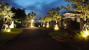 A pathway leading to a building with multiple rooms, surrounded by trees and illuminated by artificial lighting. - Bannjamjuree Resort Sattahip (Sattahip)