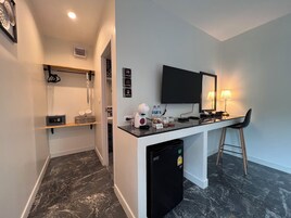 A modern hotel room with a marble floor, a small kitchenette with a refrigerator, a flat-screen TV, a desk with a chair, and a shower area with a towel rack.