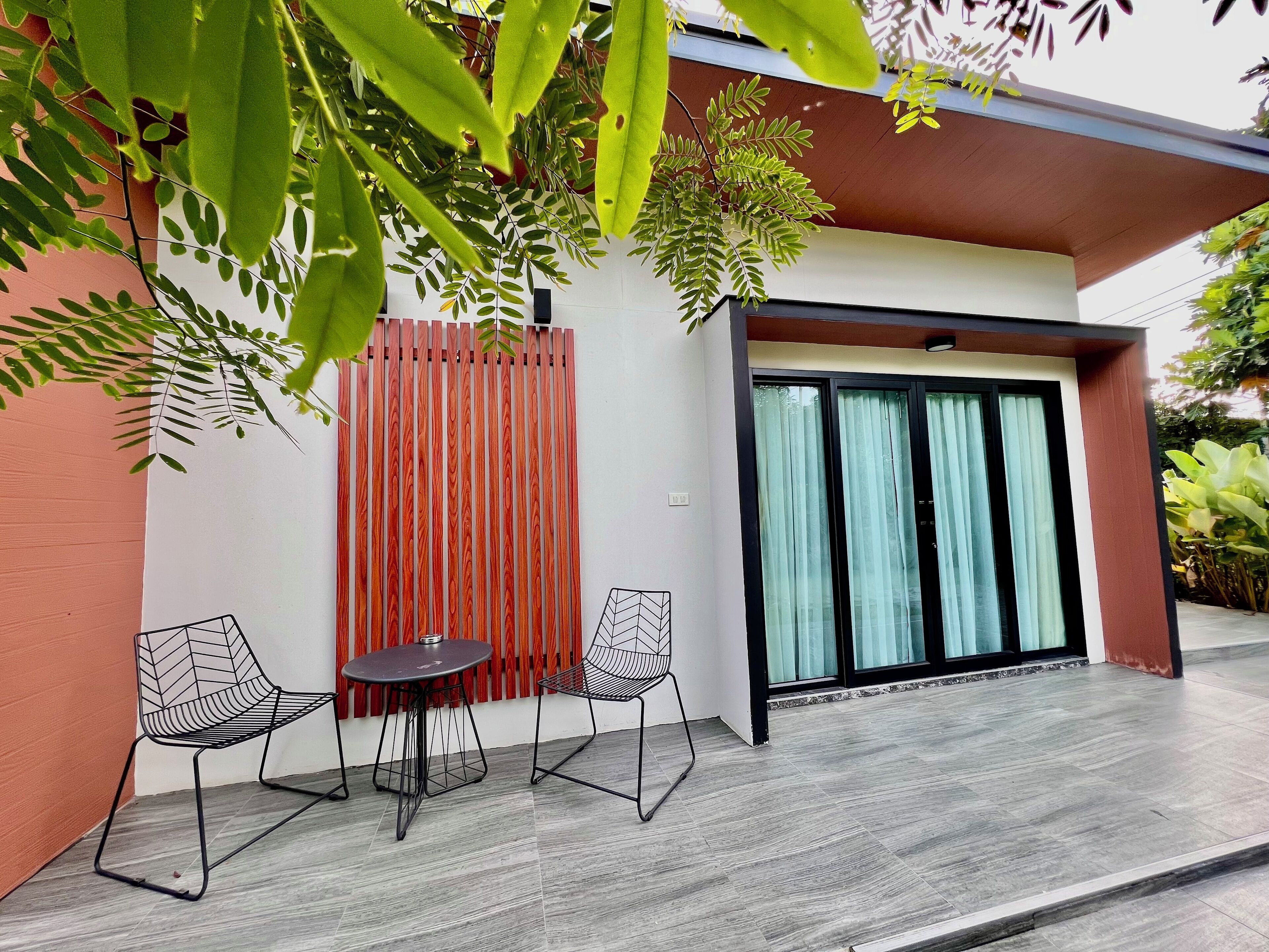 A modern outdoor seating area with two chairs and a table, a wooden fence, and a glass door leading to a covered entrance.