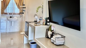 A modern living room with a large flat-screen TV mounted on the wall, a chandelier, a kitchen area with a sink and countertop, and a decorative gnome figure. - Bannjamjuree Resort Sattahip (Sattahip)