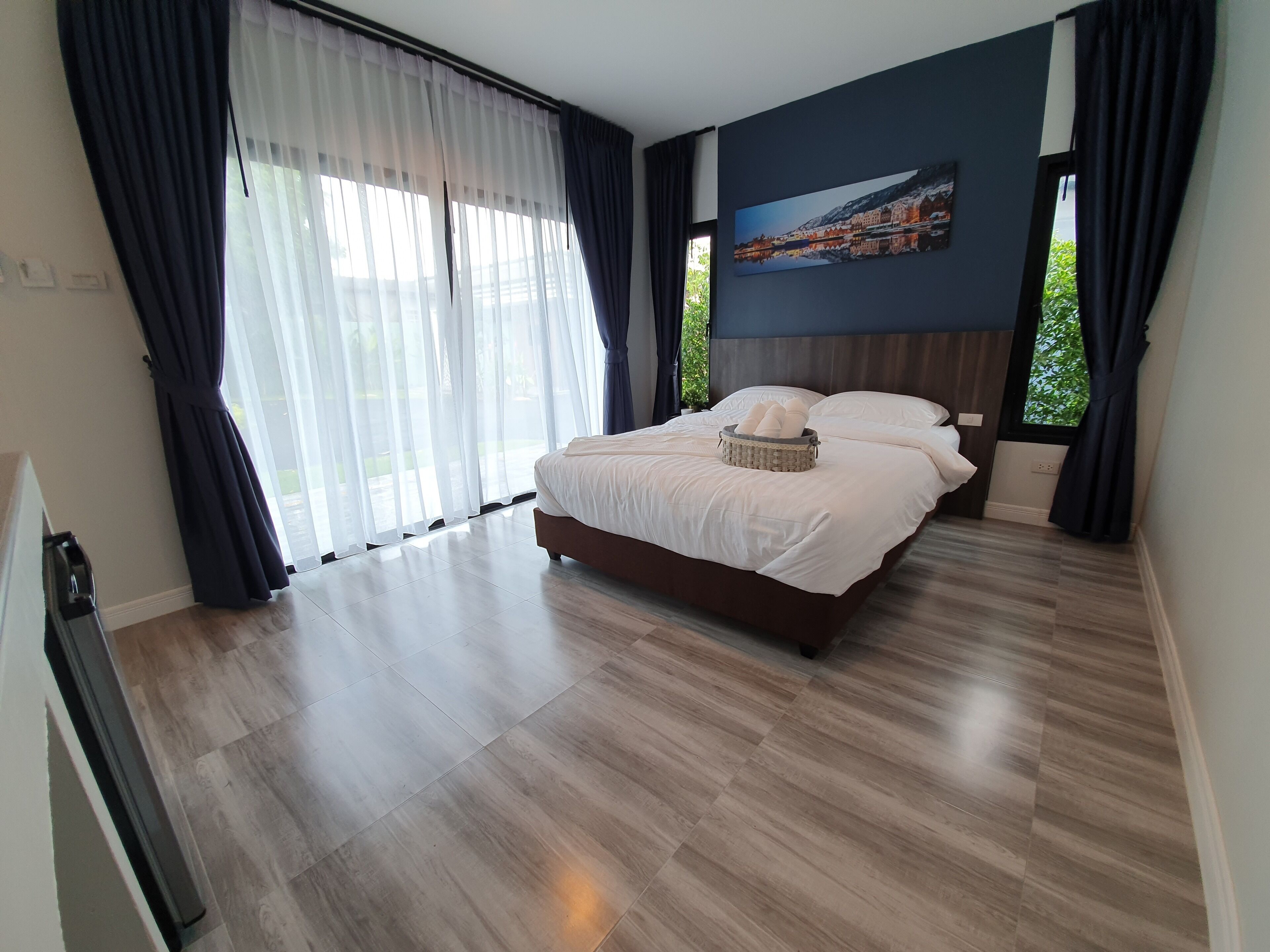 A modern bedroom with a large bed, a view of a cityscape through the window, and a wooden floor.